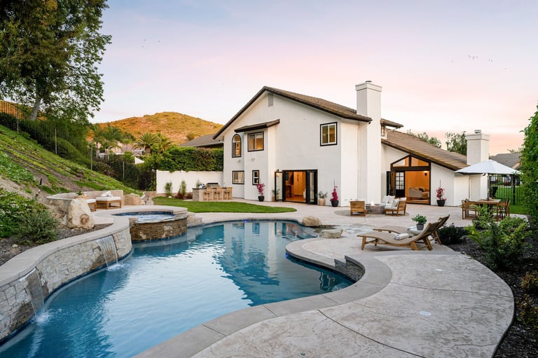 A luxurious backyard with a swimming pool, hot tub, and patio furniture at a modern house during sunset