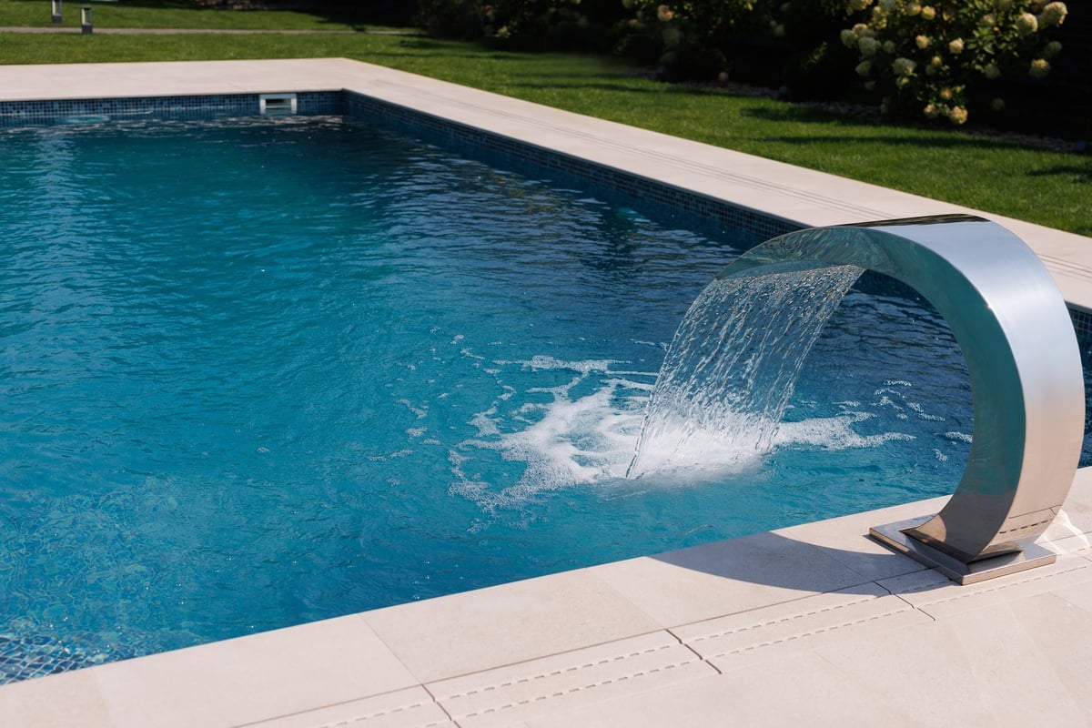 Luxury outdoor swimming pool with a modern stainless steel waterfall feature, creating a refreshing and elegant summer vibe
