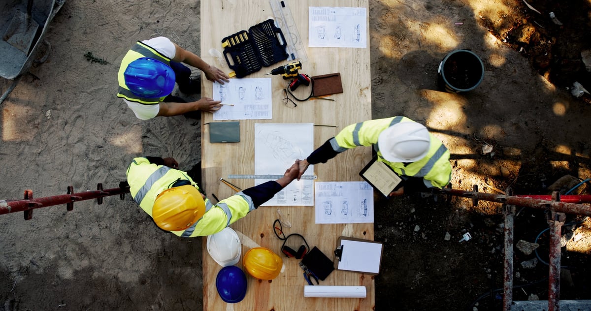Business professionals shaking hands over construction blueprints, partnership and collaboration