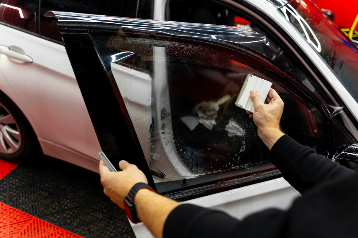 Detailer apply dark tint film to car side windows using a squeegee for smooth, bubble-free adhesion