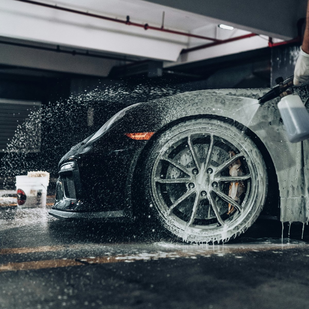 Black car being washed with high-pressure water spray at an indoor car wash facility
