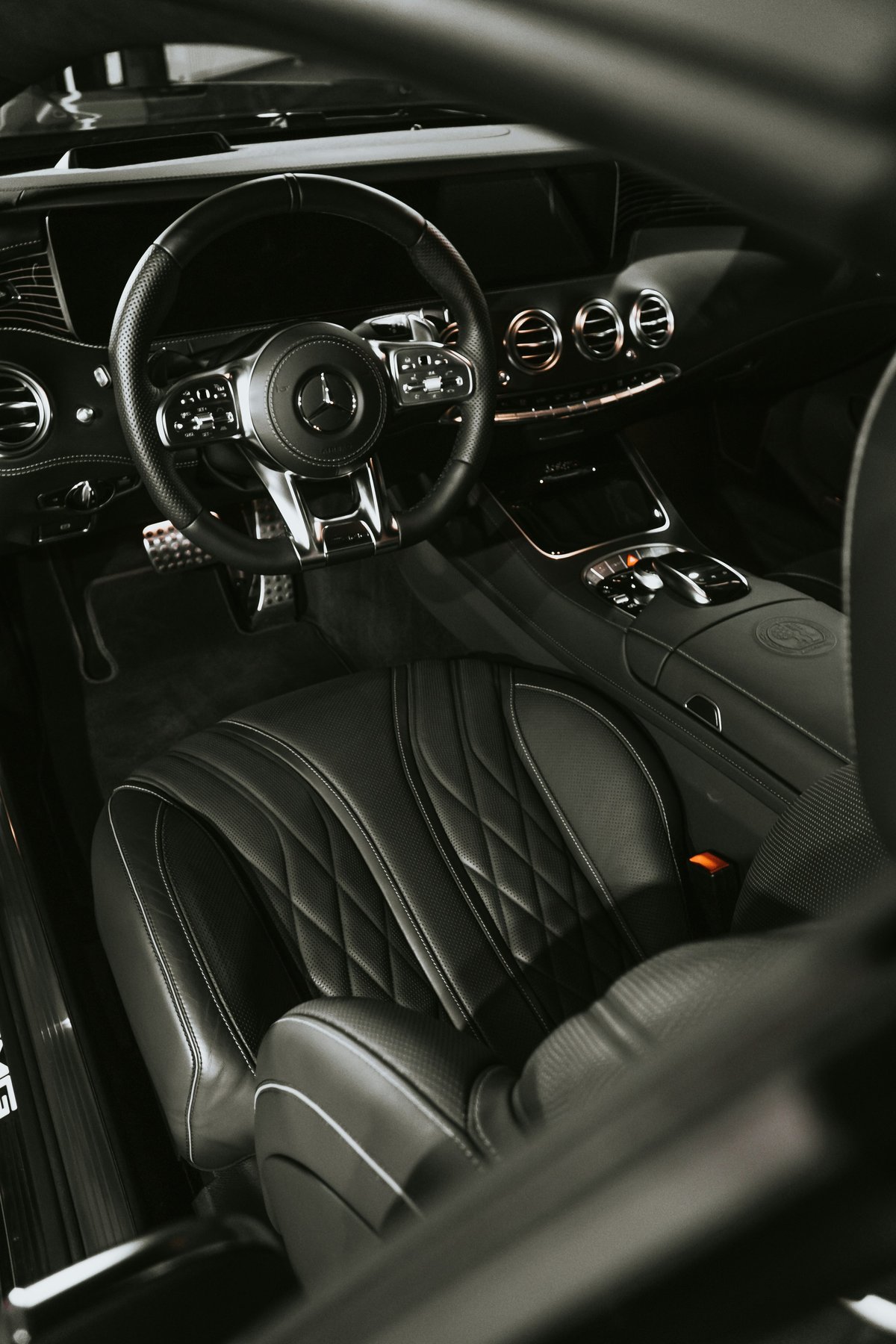 Black luxury car interior with leather steering wheel, quilted seats, and illuminated dashboard controls