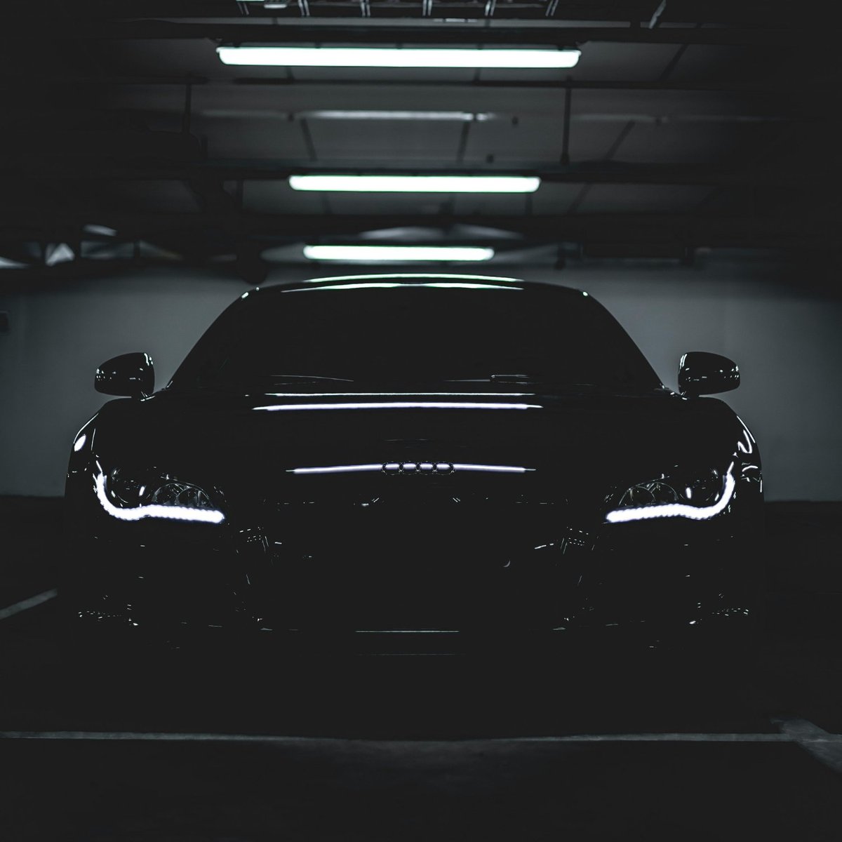 Black sports car front view in a dark garage with LED headlights illuminated and ceiling lights above