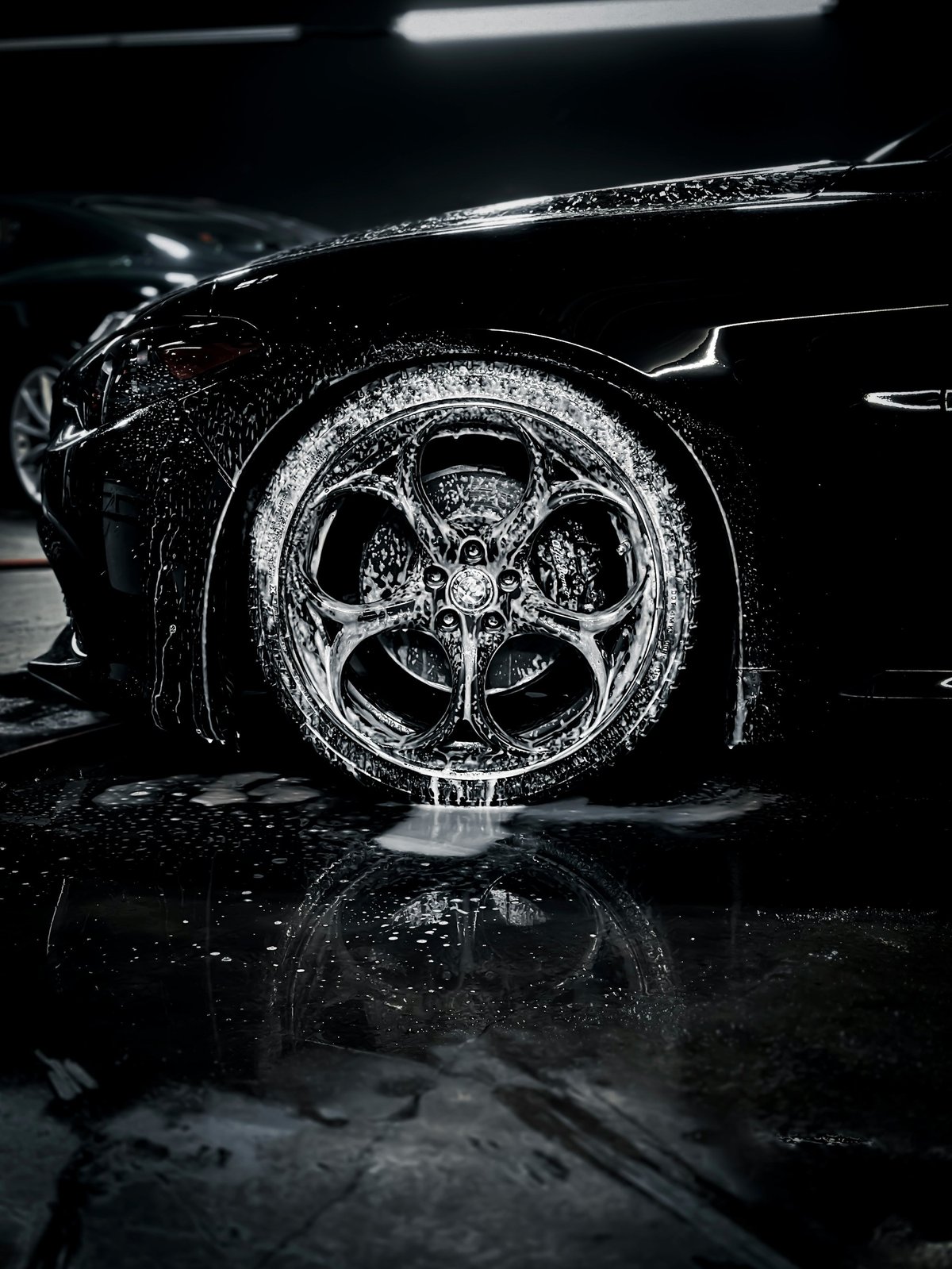 Close-up of wet car wheel and tire with intricate alloy rim design, dramatically lit against dark background
